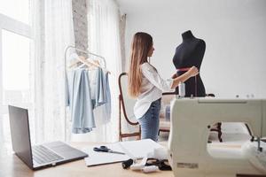 proceso de medir el ancho del maniquí. diseñadora de moda femenina trabaja en la ropa nueva en el taller foto