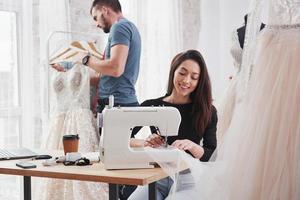 es importante amar tu trabajo. diseñadora de moda femenina trabaja en la ropa nueva en el taller con el hombre detrás foto