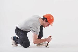 el hombre con ropa informal y sombrero duro de color naranja tiene trabajo usando un martillo. Fondo blanco foto