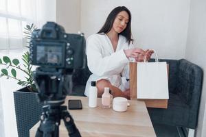 Delivery arrived. In front of camera on the tripod. Conception of fashion and skincare. Brunette girl uses cosmetics photo