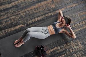 Stylish wooden floor. Top view of girl with slender body works on the abs when lying on the floor photo