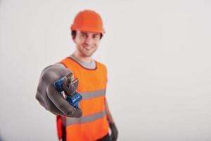 toma esta herramienta. hombre con uniforme de color naranja se alza contra un fondo blanco en el estudio foto