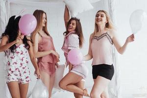 Let's go crazy. Standing on the luxury white bad at holiday time with balloons and bunny ears. Four beautiful girls in night wear have party photo