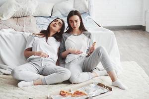 Overeating is never good. Twins have full stomach with pizza. Nice bedroom at daytime photo