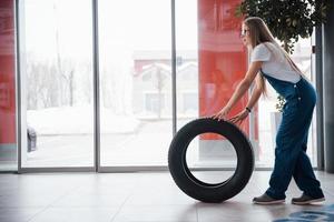 Automatic doors is in the front. Woman walks with brand new wheel to the car. Conception of repair photo