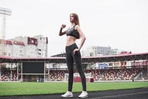 foto de altura completa. joven rubia calentándose en la pista en el estadio durante el día