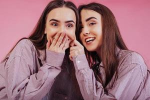 Playing and having fun with each other. Two sisters twins standing and posing in the studio with white background photo