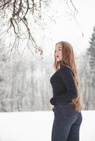 With hands in the pockets. Pretty girl with long hair and in black blouse is in the winter forest photo