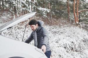 Unexpected situation. Guy stuck in the winter forest because his car have some problems. Tries to repair automobile photo