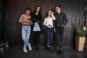 Nice clean room with plant on the right side. Youth stands against black wooden wall. Group of friends spending time together photo