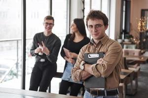 Holds notepad. Group of students in eyewear standing in the learning room with documents photo