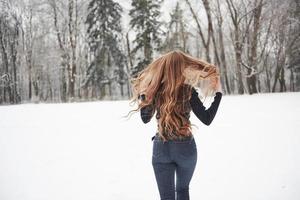 Hair to the different sides. Rear view of girl with long hair runs near the forest to the automobile in wintertime photo