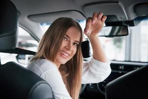 Ahora es mio. hermosa chica rubia sentada en el auto nuevo con interior negro moderno foto