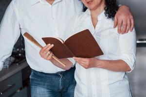 Close up view of a book. Man and his wife in white shirt preparing food on the kitchen using vegetables photo