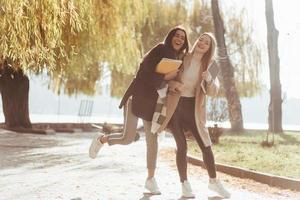 Cheerful atmosphere. Two young friends are glad to meet each other at park after the studying photo