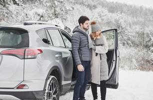 Happy people near the car looking at beautiful nature landscapes. Lovely couple have weekend at countryside at winter time photo