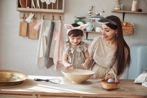 Process of learning how to prepare food. Mother and daughter in bunny ears at easter time have some fun in the kitchen at daytime photo