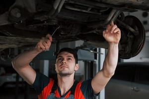 Front view. Man at the workshop in uniform fixes broken parts of the modern car photo