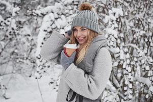 Joyful mood. Portrait of cute blonde in warm clothes that enjoying spending her weekend outdoors in the winter forest photo