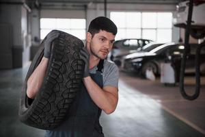 Short haired unshaved man. Mechanic holding a tire at the repair garage. Replacement of winter and summer tires photo