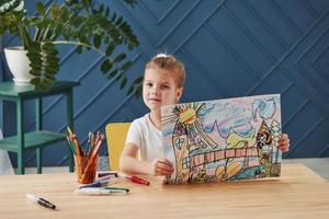 Take a look at that picture. Cute little girl in art school shows her first paintings drawn by pencils and markers photo