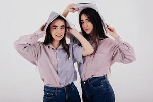 Students have fun at their break. Two sisters twins standing and posing in the studio with white background photo