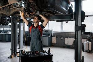 Artificial and natural lighting. Man at the workshop in uniform fixes broken parts of the modern car photo