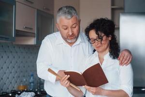 Learning some new stuff. Man and his wife in white shirt preparing food on the kitchen using vegetables photo