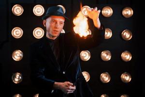 Controlling the flame. Professional magician showing trick. Light bulbs on background photo