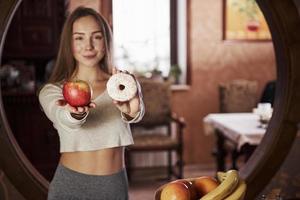 galleta y manzana en las manos. bastante joven de pie en la cocina moderna cerca de la estufa de gas foto