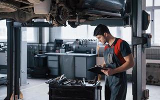 Nice looking autosalon. Man at the workshop in uniform using notepad for his job for fixing broken car photo