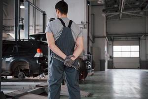 Wathing at the cars. Rear view of worker in uniform that stands in workshop with wrench in hand photo