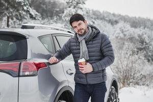 Portrait of car owner that standing near his automobile with cup of coffee in the hand at snowy winter day photo