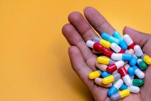 Man hand holding colorful capsule pills on yellow background. Prescription drugs. Drug overuse and polypharmacy concept. Drug allergy. Pharmaceutical industry. Pharmacy banner. Healthcare and medicine photo