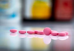 Pink tablets pills on blurred background of drug bottle in drugstore or pharmacy department in hospital. Pharmaceutical industry. Pharmaceutics concept. Medicine for treatment illness. Healthcare. photo