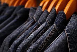 Selective focus on jacket jeans hanging on rack in clothes shop. Denim jeans with jeans pattern. Textile industry. Jeans fashion and shopping concept. Clothing concept. Denim jacket on rack for sale. photo