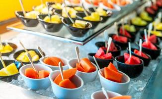 Tropical fruit buffet at event in restaurant. Catering food. Fresh papaya, watermelon and pineapple slices in small bowl on crushed ice on luxury table. Banquet service. Fruit buffet catering concept. photo