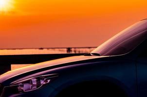 Side view of SUV car with sport and modern design parked on concrete road by the sea at sunset. Hybrid and electric car technology. Travel on vacation at the beach. Road trip. Automotive industry. photo