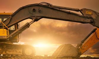 Backhoe parked at construction site after digging soil. Bulldozer on sunset sky and clouds background. Digger after work. Earth moving machine at construction site at dusk. Digger with dirt bucket. photo