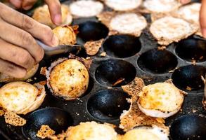 Mortar-toasted pastry or Kanom Krok is Thai traditional dessert. Woman hand removing Kanom Krok from stove by spoon. Street food in Thailand. Thai dessert made from coconut milk and flour. photo