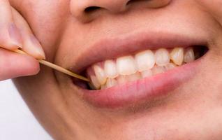 una mujer asiática se limpia los dientes de la comida y se pega los dientes con un palillo de madera de bambú después del desayuno, el almuerzo y la cena. cuidado dental personal con estilo asiático. concepto de problema de salud dental y mal aliento.