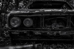 Old wrecked car in black and white scene. Abandoned rusty car in the forest. Closeup front view of decayed and rusty wrecked abandoned car. The art of abandoned used car. Tragedy and loss. Sadness photo
