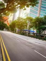 carretera asfaltada vacía en la ciudad. ciudad verde con rascacielos moderno edificio de oficinas. edificio de cristal del centro financiero y de negocios. paisaje urbano árbol verde al lado de la carretera para reducir el polvo y la contaminación del aire. foto