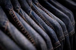 Selective focus on jacket jeans hanging on rack in clothes shop. Denim jeans with jeans pattern. Textile industry. Jeans fashion and shopping concept. Clothing concept. Denim jacket on rack for sale. photo