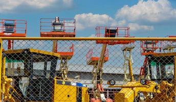 Mesh fence of outdoor warehouse parking lot of articulated boom lift and motor grader. Machine for renting in construction and mining industry. Blur construction crane and motor grader for rent. photo