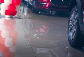 Selective focus on Wheel and tires of new red car parked in modern showroom with reflection on tile floor and balloons. Car dealership concept. Sales promotion in showroom. Automobile industry crisis. photo