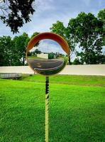 Convex safety mirror mounted on traffic pole at road curve. Asphalt road reflected in mirror. Safety device for dangerous and narrow sharp curve road. Bike lane and walkway sign on the road at park. photo