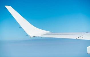 Wing of plane over white clouds. Airplane flying on blue sky. Scenic view from airplane window. Commercial airline flight. Plane wing above clouds. Flight mechanics concept. International flight. photo