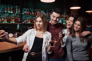 Guy hugs every girl. Friends taking selfie in beautiful nightclub. With drinks in the hands photo