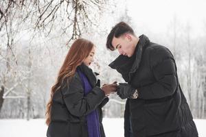 Coffee in hands. Gorgeous young couple have good time together in snowy forest photo
